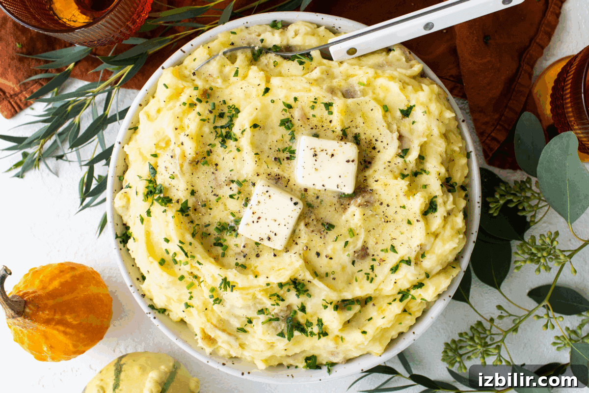 Thanksgiving Sides Worth Serving (Everything But Turkey) 2 A bowl of mashed potatoes topped with two pats of butter, chopped herbs, and ground pepper sits amid autumn-themed decorations—one of the best Thanksgiving sides for your holiday table.