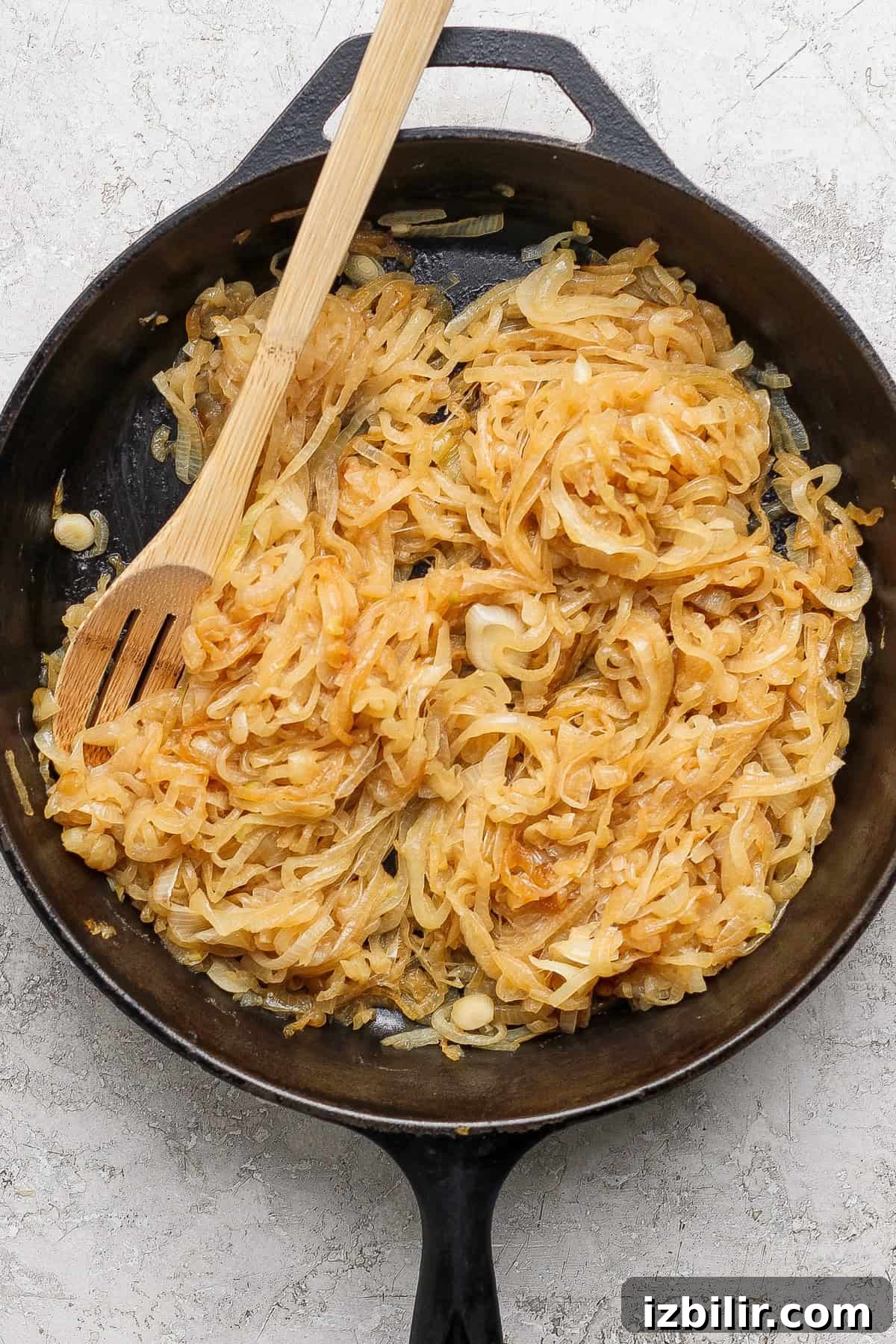 Creamy Mashed Potatoes with Caramelized Onions Recipe 4 Sliced onions caramelizing in a black cast iron skillet with a wooden spoon resting on top.