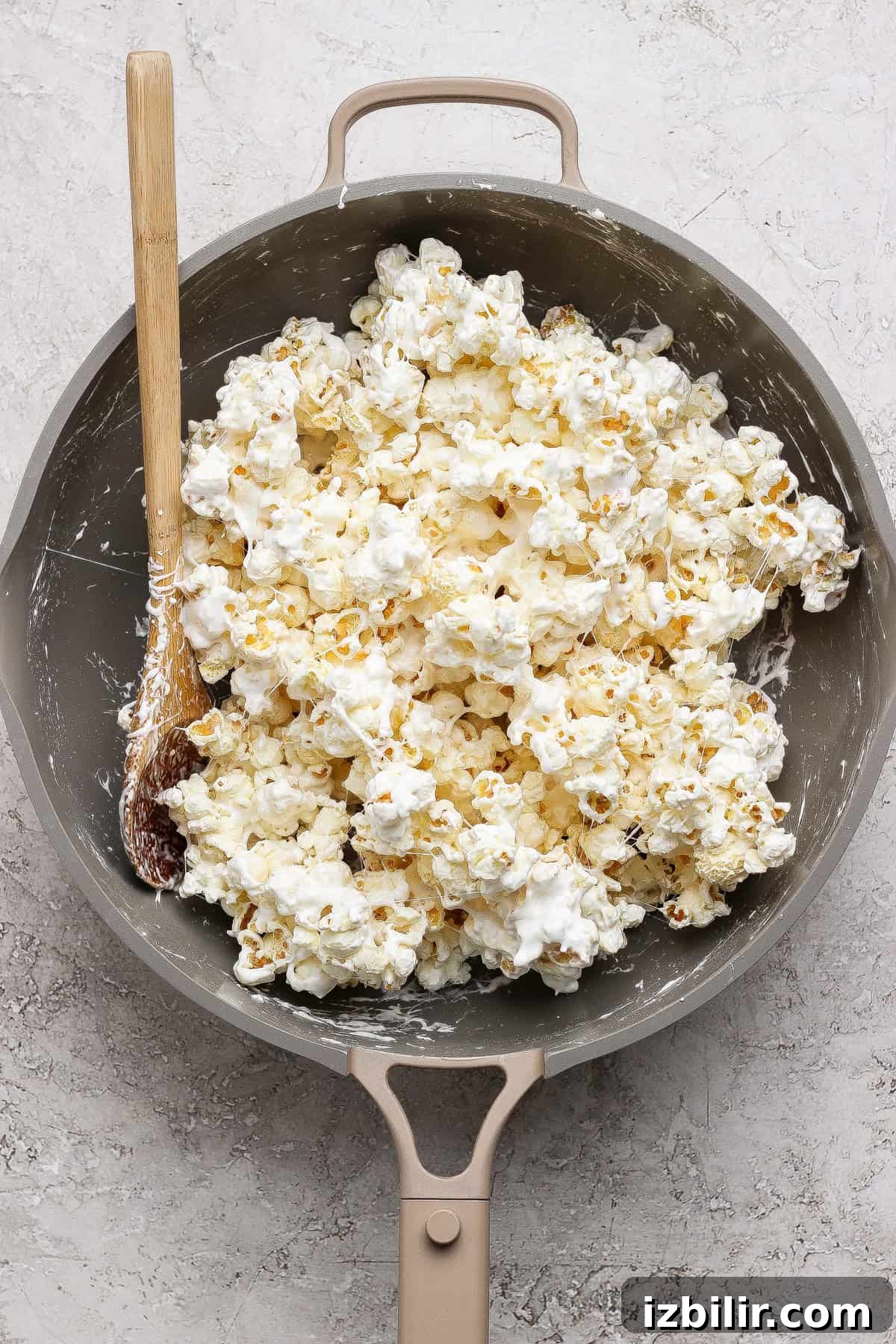 A pan filled with popcorn coated in a white, sticky mixture, with a wooden spoon resting on the side.