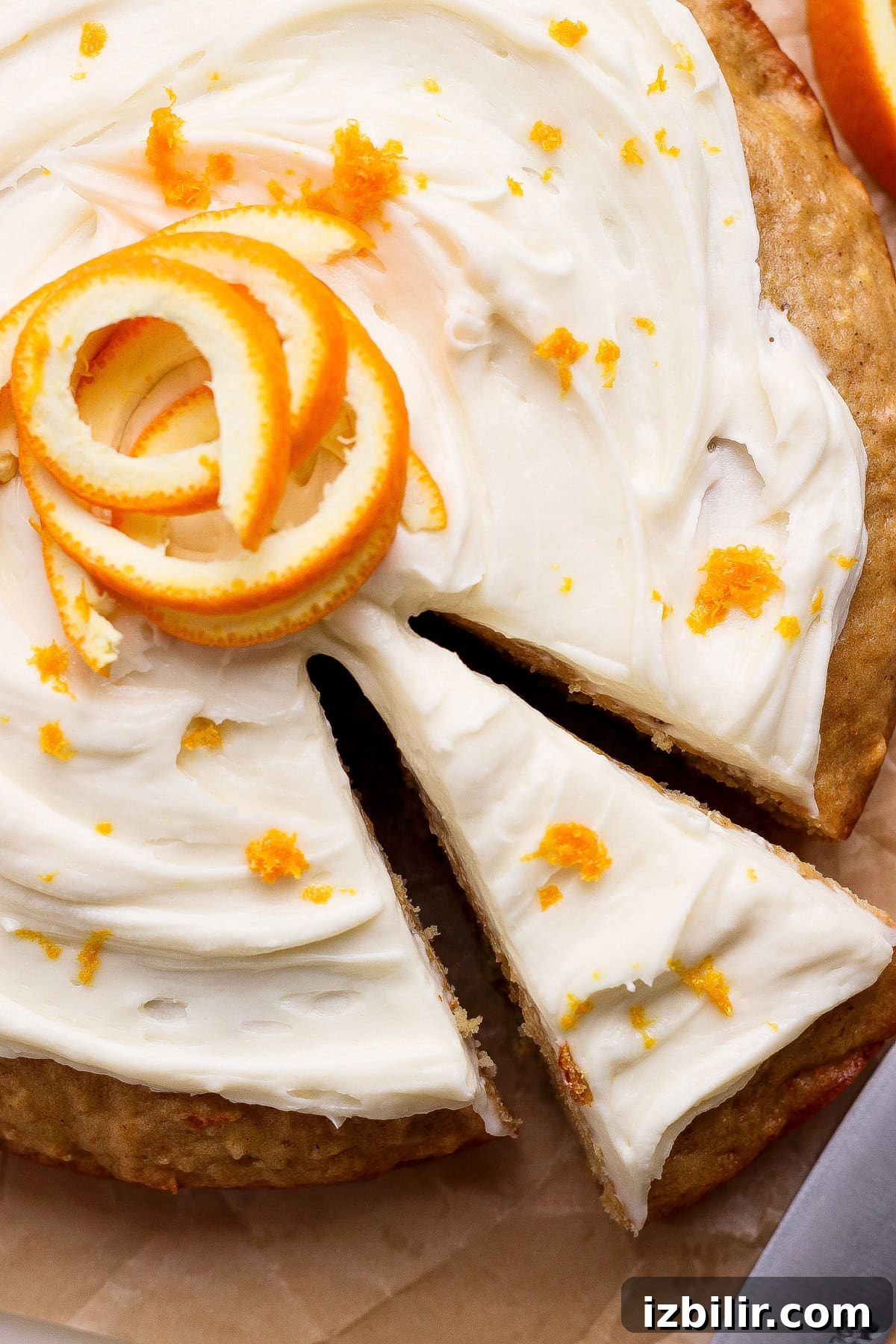 A round cake with white frosting, garnished with orange zest and a spiral of orange peel, with one slice being separated from the whole cake.