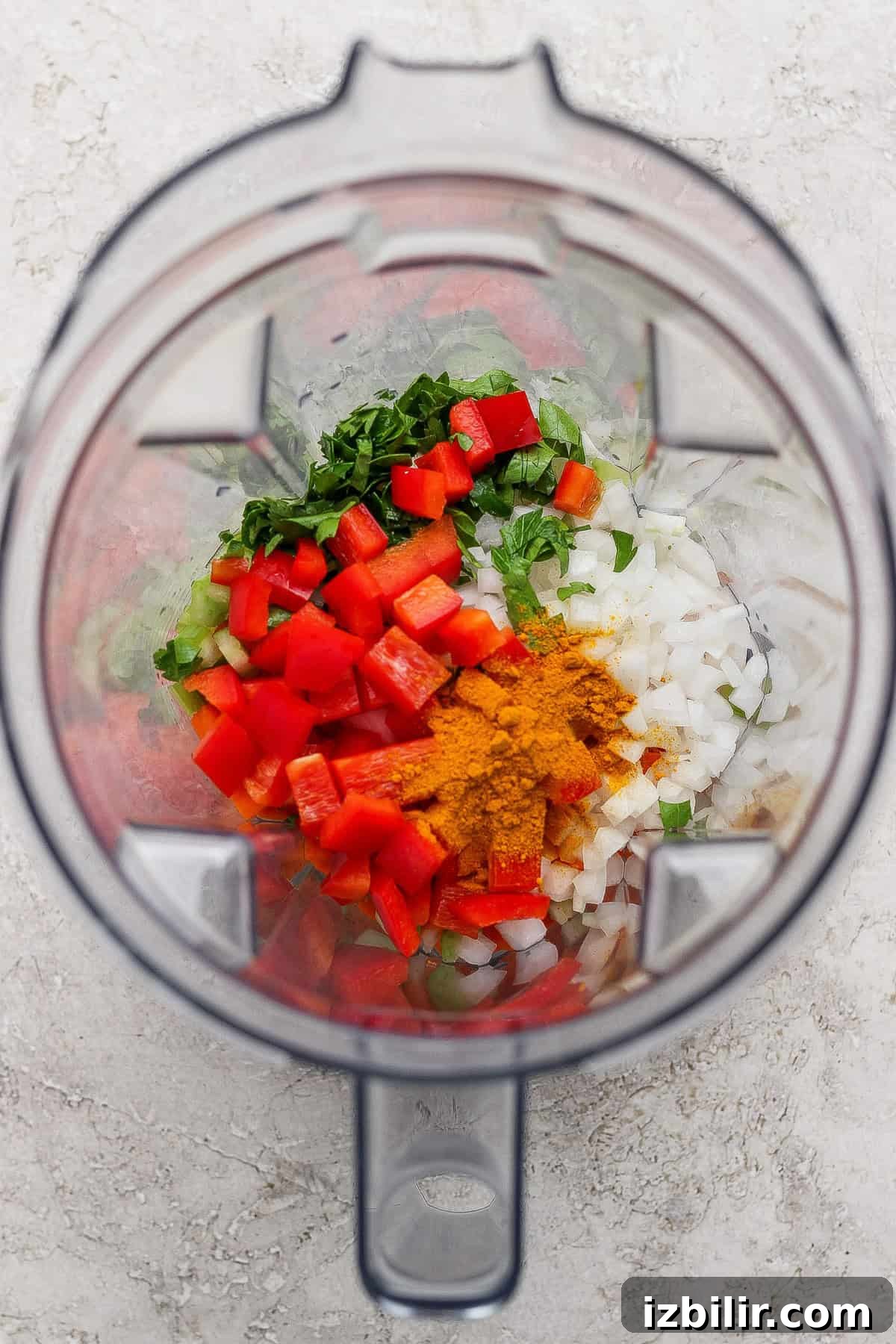 Comforting Soup to Boost Immunity 3 A blender filled with chopped red bell pepper, onion, green herbs, and a bright yellow spice on a light-colored surface.