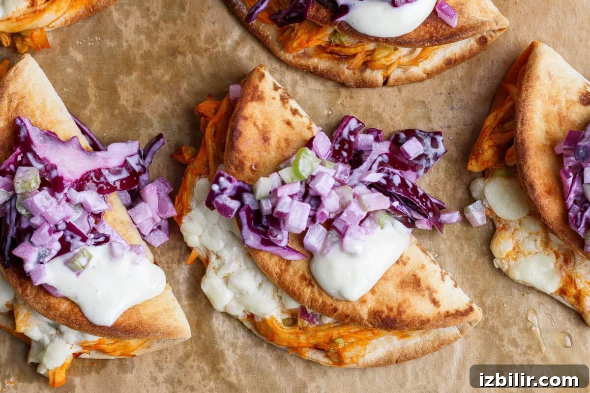 Three folded flatbreads filled with shredded meat, melted cheese, sauce, and topped with chopped red onions and purple cabbage on parchment paper.