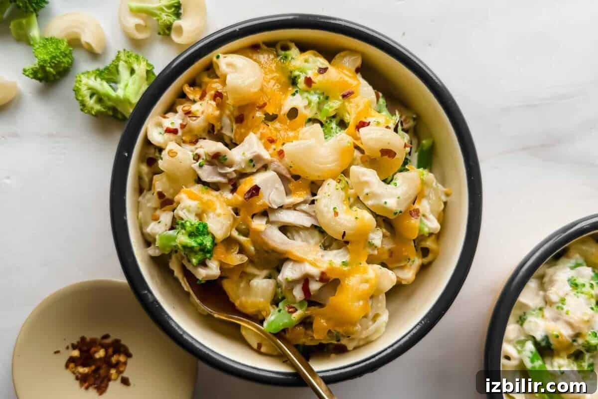 Creamy Chicken and Broccoli Mac with Cottage Cheese 2 A bowl of macaroni and cheese with broccoli, topped with melted cheese and red pepper flakes, with a spoon in the bowl.