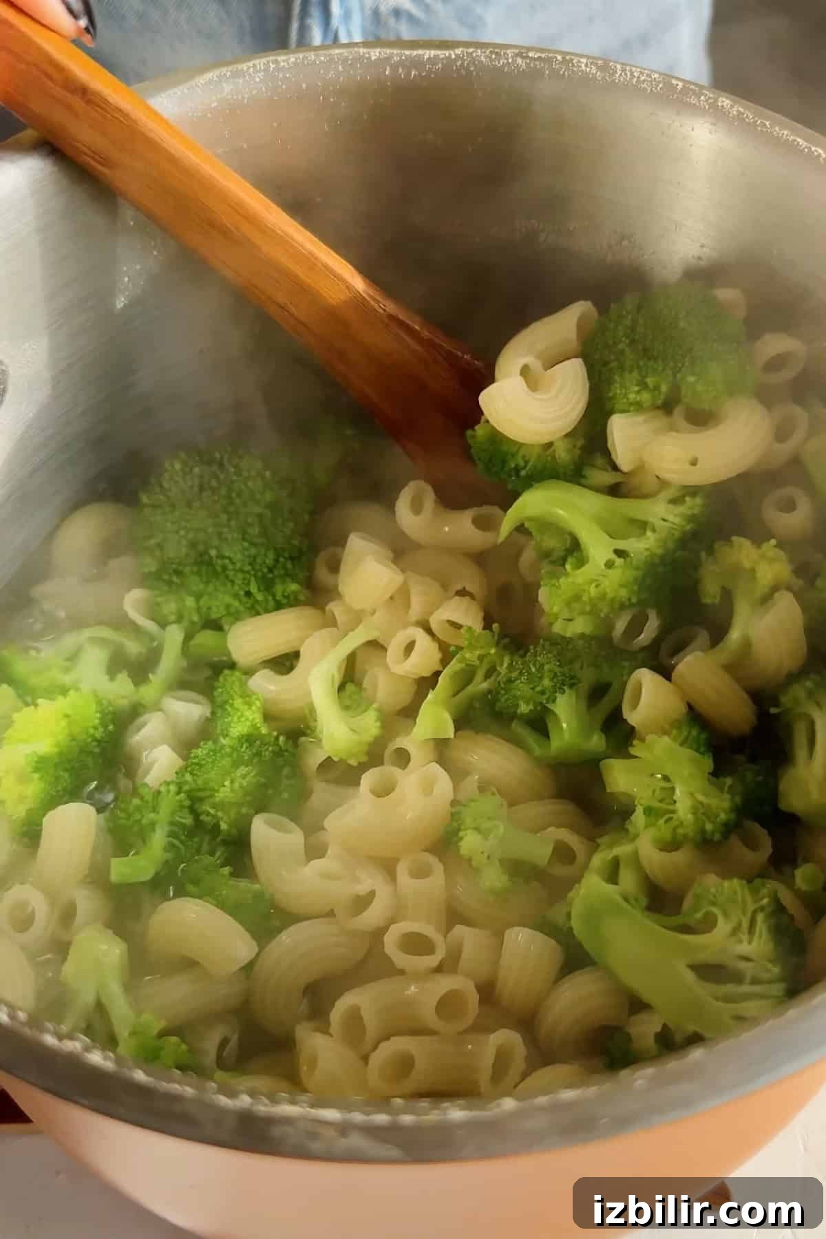 Creamy Chicken and Broccoli Mac with Cottage Cheese 3 A pot of cooked pasta and broccoli being stirred with a wooden spoon, with steam rising.