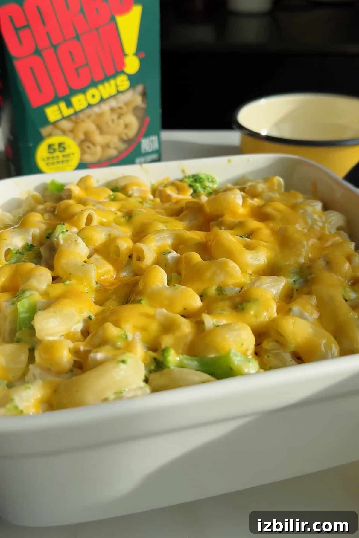 Creamy Chicken and Broccoli Mac with Cottage Cheese 5 A white dish filled with macaroni and cheese topped with melted cheese and broccoli; a box of elbow pasta and a cup are in the background.