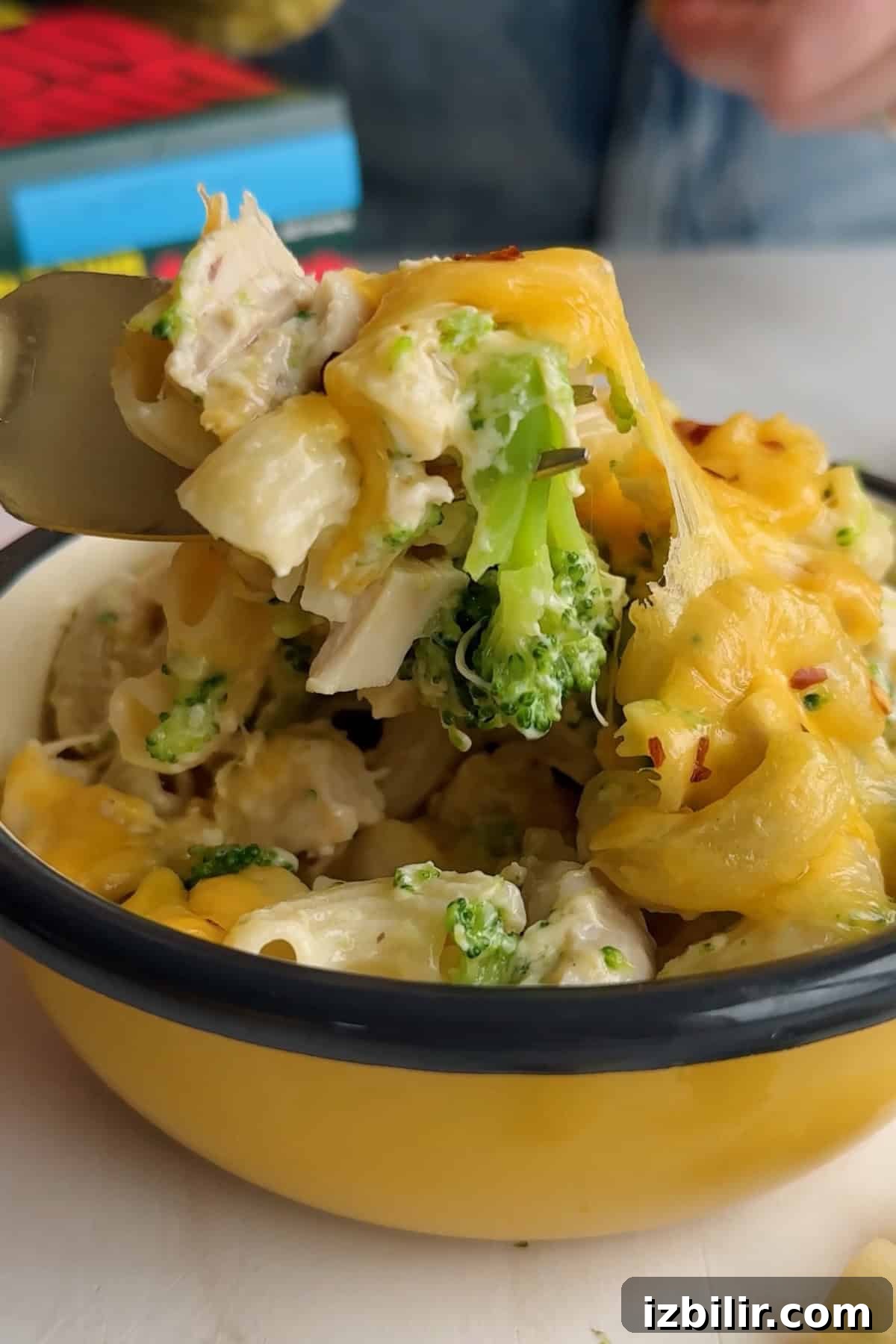 Creamy Chicken and Broccoli Mac with Cottage Cheese 6 A fork lifts a portion of cheesy pasta with broccoli and chicken from a yellow enamel bowl.