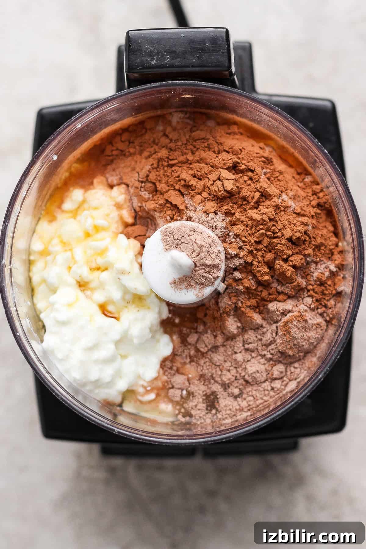 Single Serve Cottage Cheese Brownie Recipe for One 3 Top view of a food processor bowl containing cottage cheese, cocoa powder, protein powder, and other ingredients before blending.