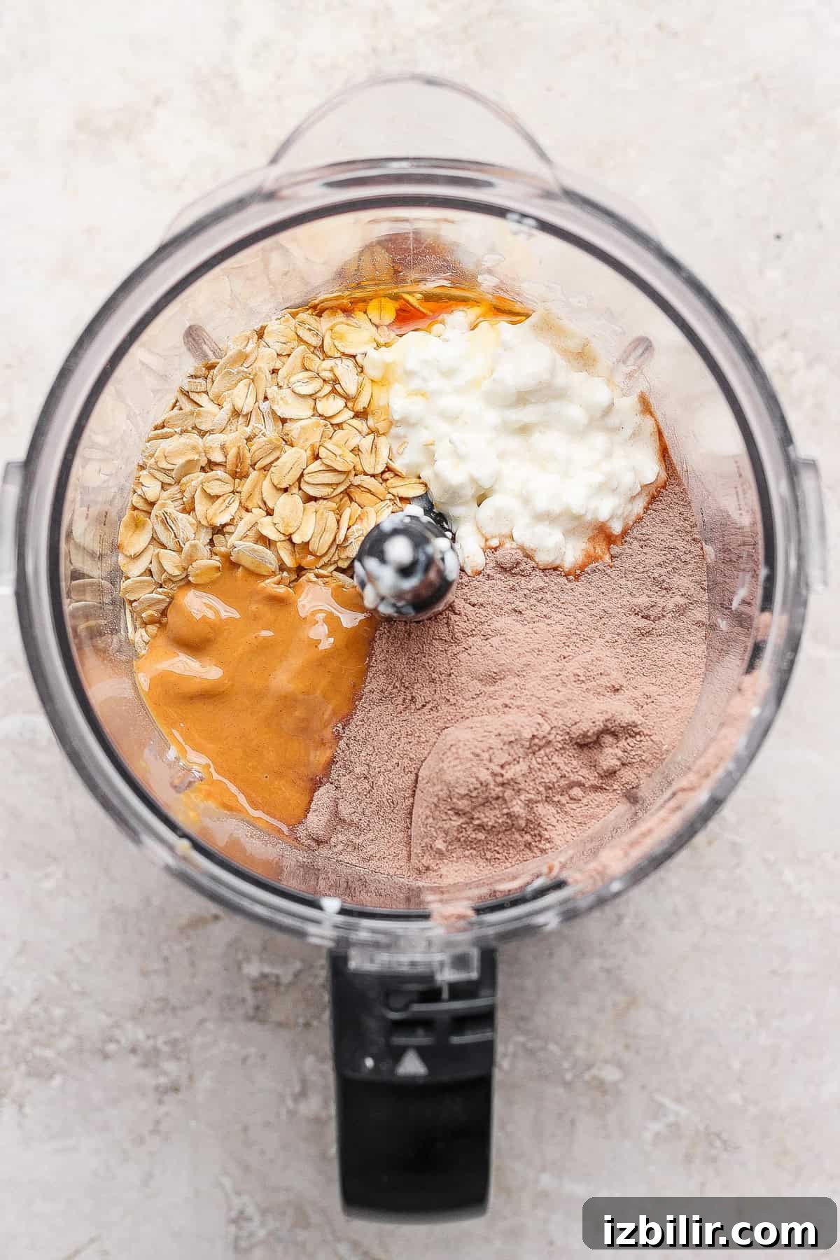 No-Bake Cottage Cheese Cheesecake Bars Recipe 4 Top-down view of a food processor bowl containing oats, cocoa powder, cottage cheese, peanut butter, and an egg, ready to be blended.