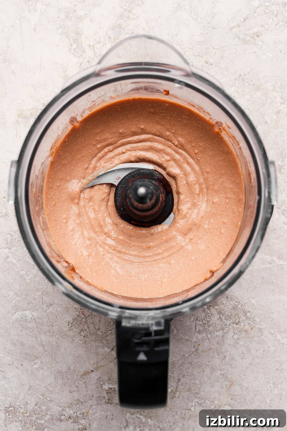 No-Bake Cottage Cheese Cheesecake Bars Recipe 5 A food processor filled with a smooth, light brown mixture, shown from above on a light-colored surface.