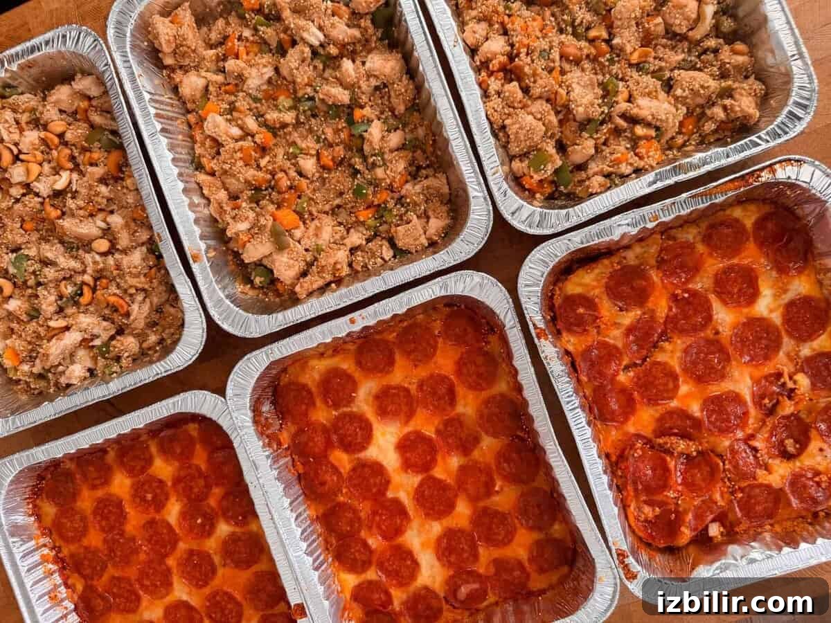 Several aluminum trays with pizza and vegetable chicken dishes arranged on a wooden surface