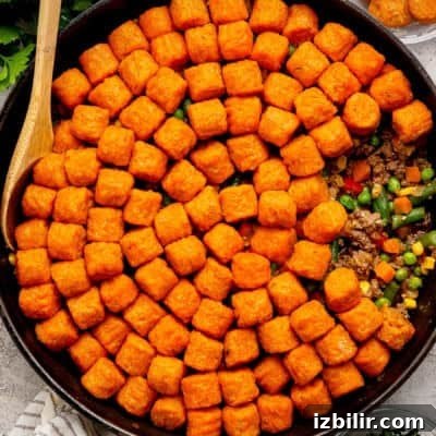 Sweet potato tater tot casserole in a skillet with a wooden spoon