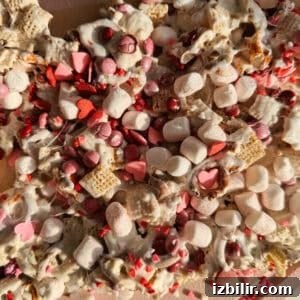Valentine's Chex Mix Recipe: Cupid's Sweet and Savory Snack 3 A close-up of a Valentine's Day snack mix with cereal squares, mini marshmallows, red and pink candy-coated chocolates, and heart-shaped sprinkles.