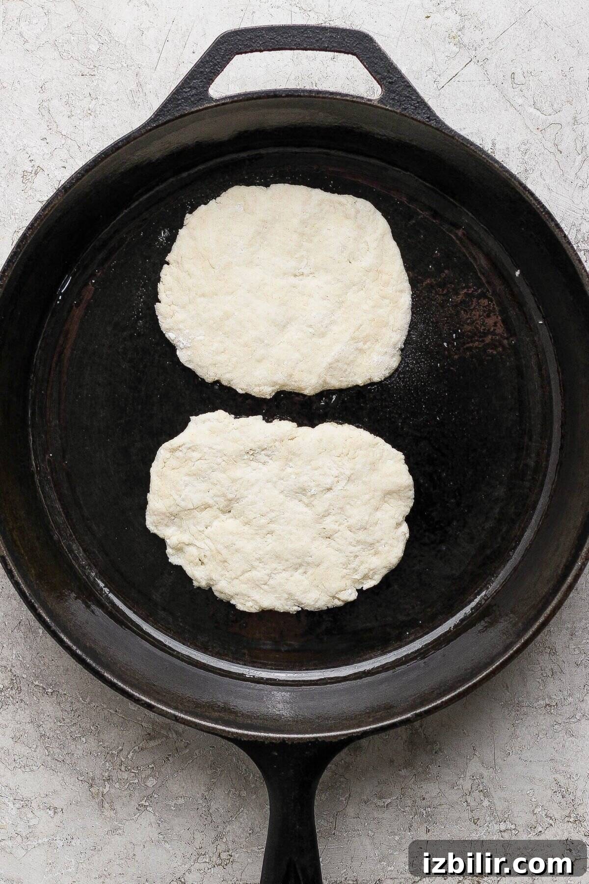 Homemade Buttery Garlic Naan Recipe with High-Protein Dough 4 Two pieces of raw garlic naan dough are placed side by side in a large black cast iron skillet on a light textured surface.