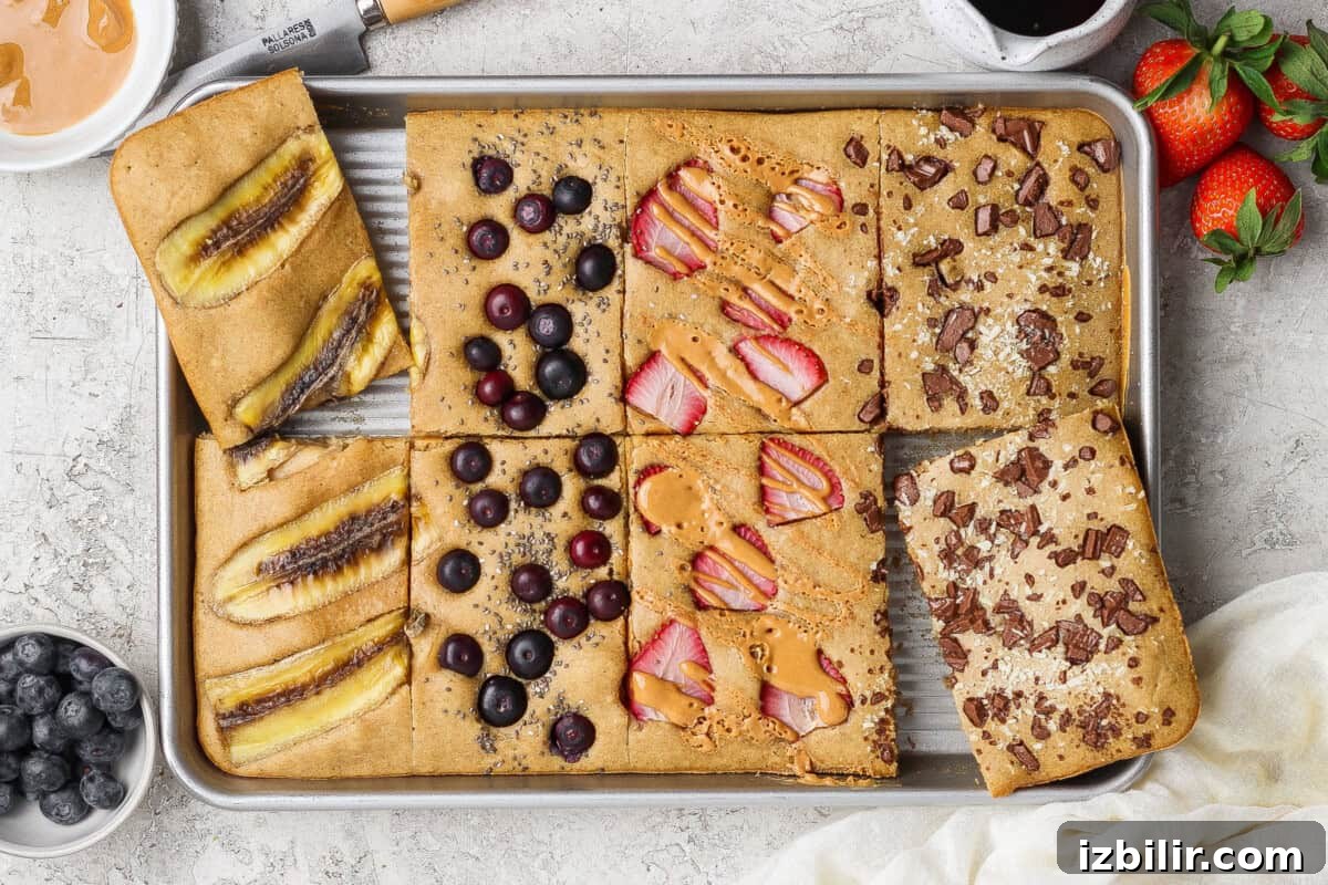 Sheet Pan Protein Pancakes Recipe - 14g Protein Per Serving 2 A sheet pan divided into six baked pancake squares, each topped with different ingredients like banana, blueberries, strawberries, peanut butter, and chocolate pieces.