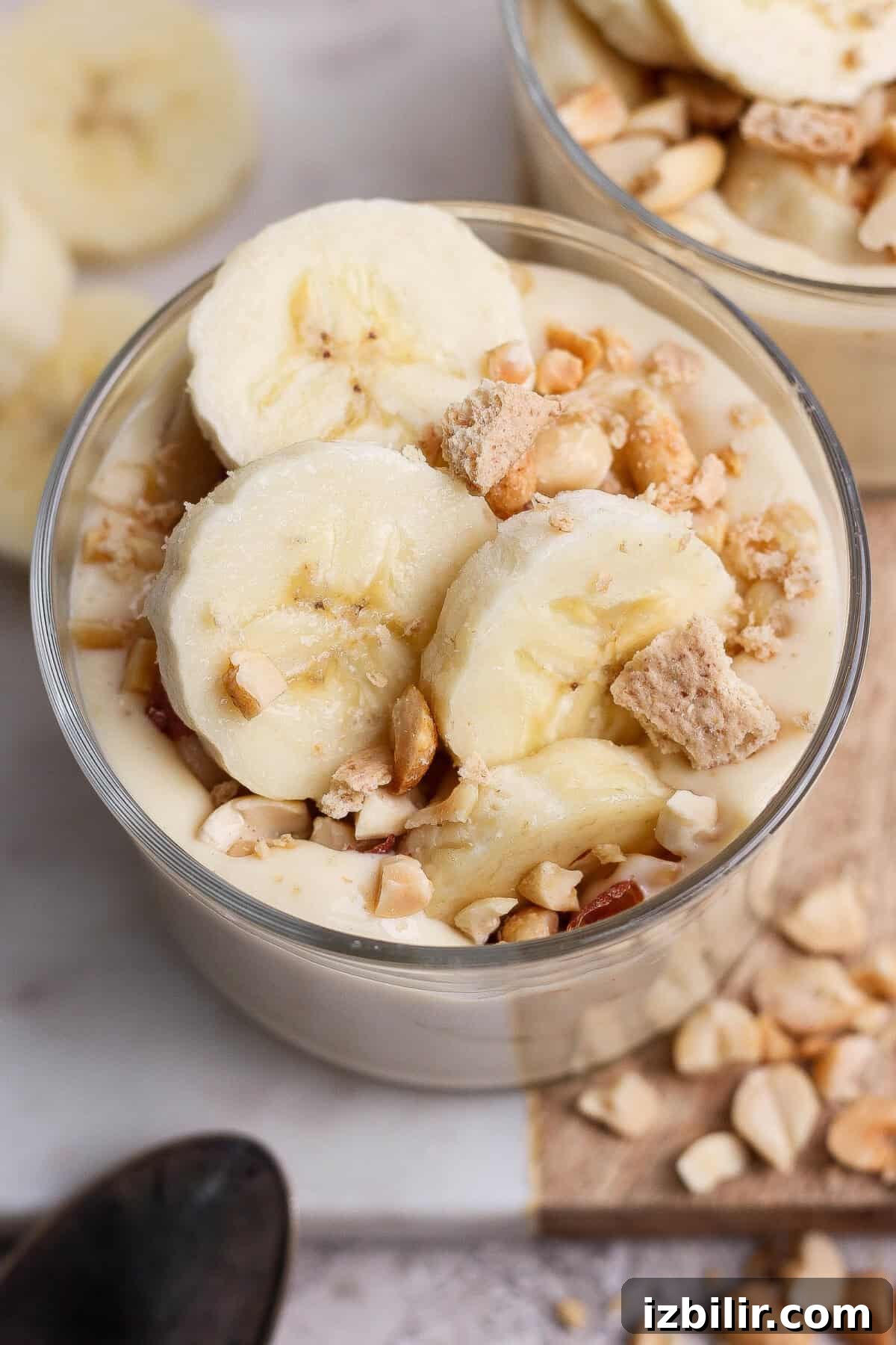 A glass bowl filled with banana pudding, topped with banana slices, chopped nuts, and cookie pieces.