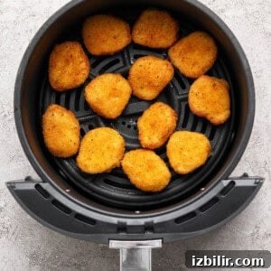 Chicken nuggets arranged in a single layer inside an air fryer basket on a light-colored surface.