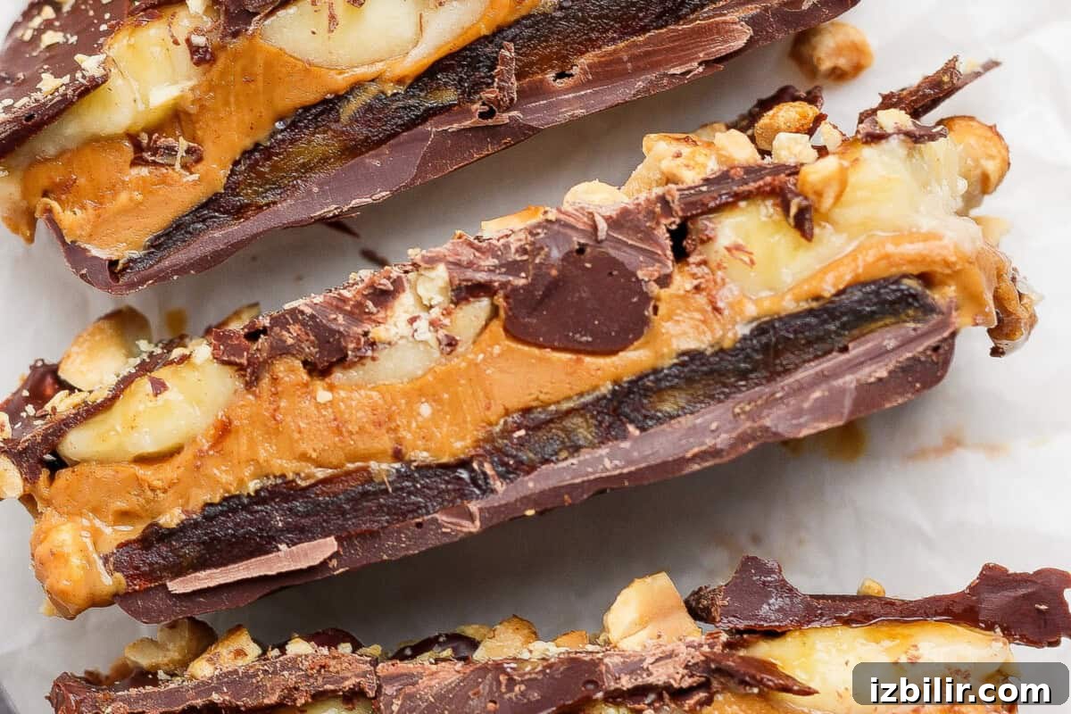 Close-up of chocolate bars layered with peanuts, caramel, and chocolate, showing a cross-section of the ingredients on a white background.