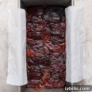 A rectangular baking pan lined with parchment paper, filled with tightly packed dates on a textured light gray surface.