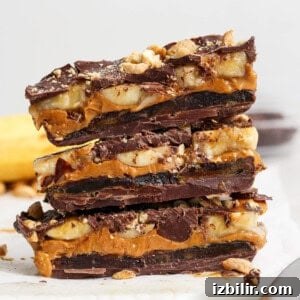 Three stacked chocolate bars filled with layers of banana, caramel, and chopped nuts, resting on parchment paper.