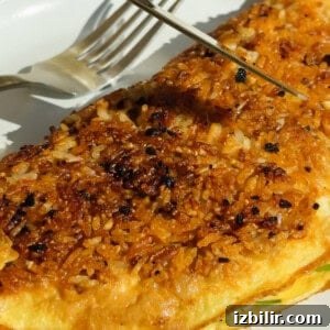 Crispy Fried Rice Omelette Recipe 6 A close-up of a golden-brown omelette topped with crispy rice on a plate, with a fork and knife positioned above it.