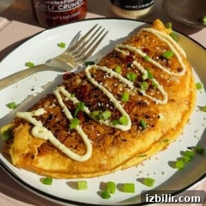 Crispy Fried Rice Omelette Recipe 7 A golden omelette filled with fried rice, topped with mayonnaise, chopped green onions, sesame seeds, and chili flakes on a white plate with a fork.