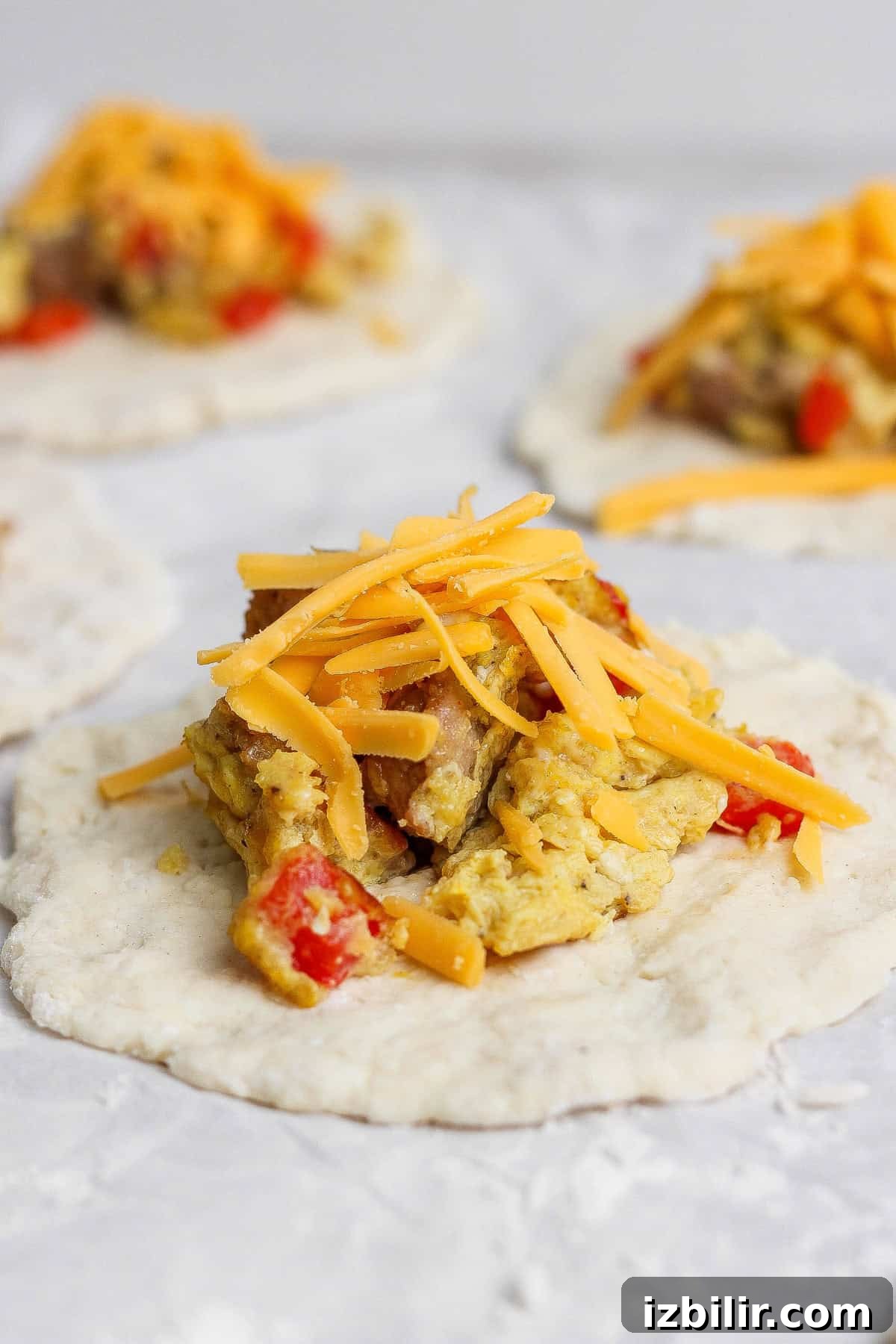 Uncooked dough topped with scrambled eggs, red bell peppers, and shredded cheddar cheese, ready to be assembled.