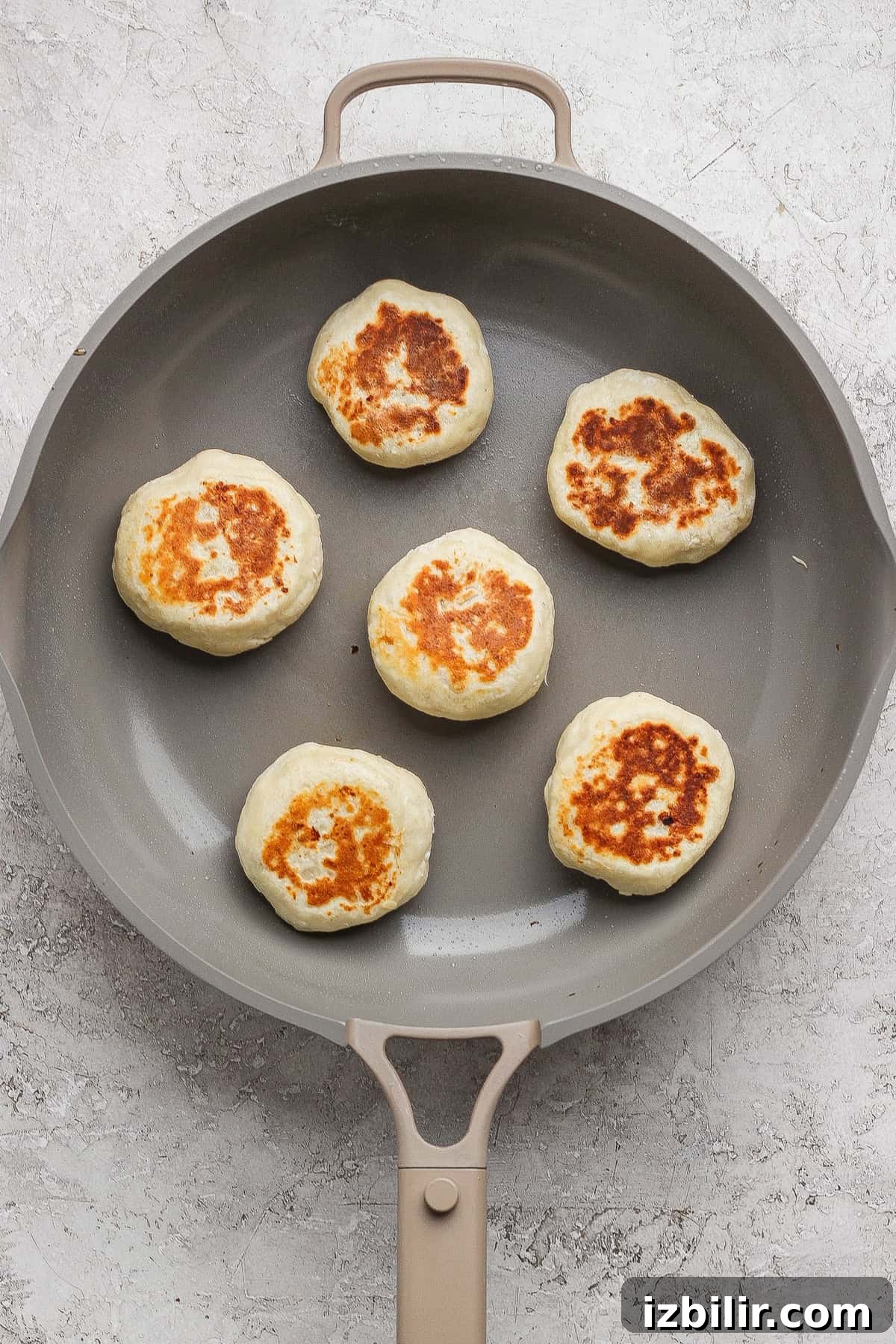 Six round, golden-brown patties are cooking in a nonstick skillet on a light-colored surface.