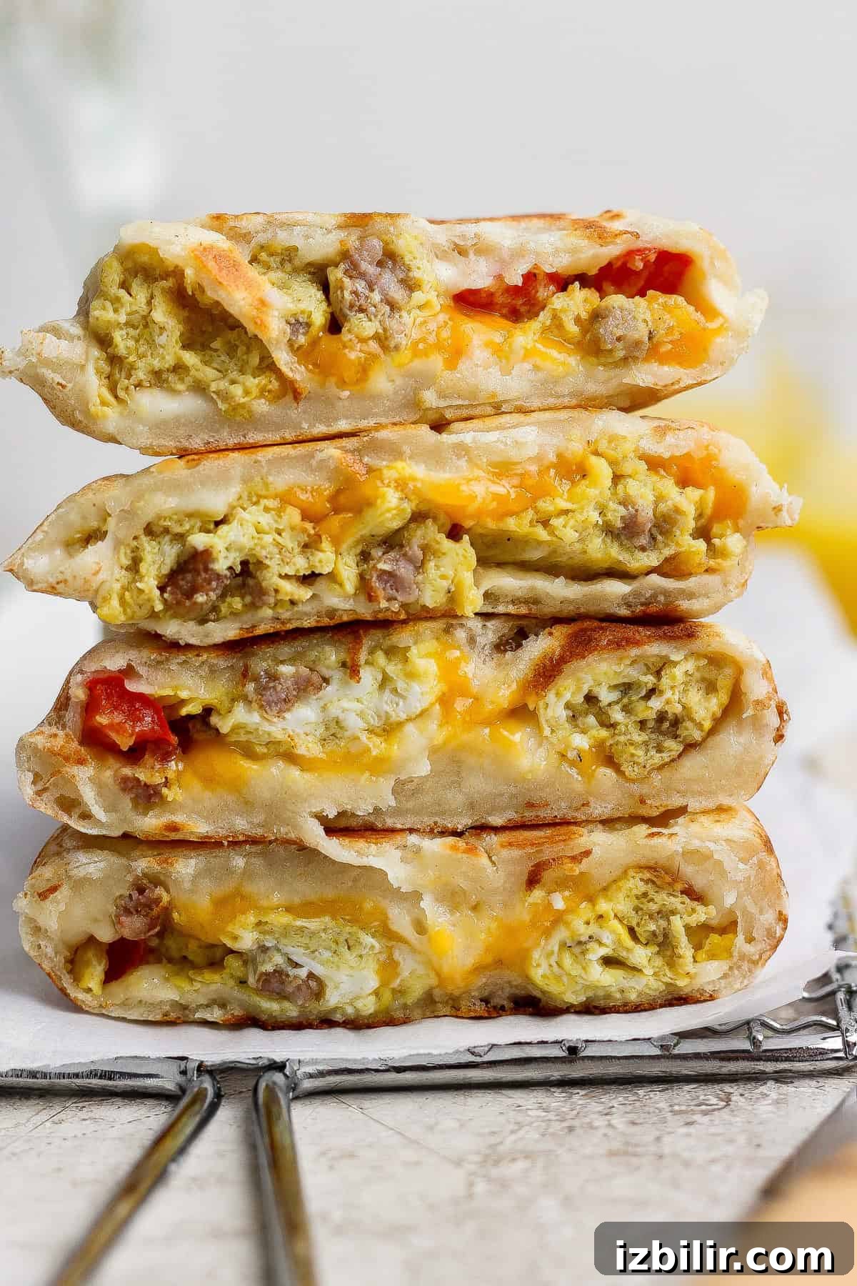 Four breakfast quesadilla wedges stacked on a cooling rack, filled with scrambled eggs, sausage, cheese, and pieces of tomato.