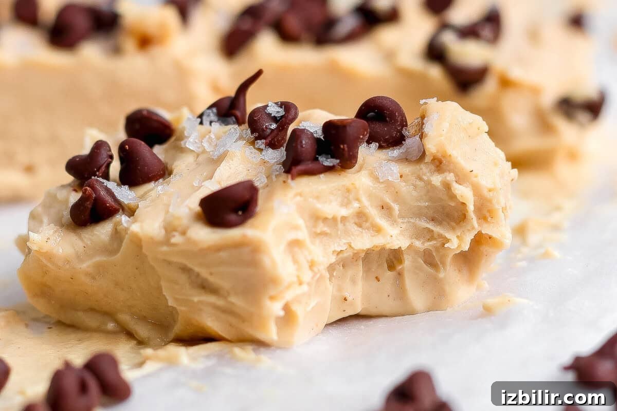 Creamy Peanut Butter Frozen Yogurt Bites Recipe 2 A creamy peanut butter fudge piece topped with chocolate chips and flaky salt, showing a bite taken out, resting on parchment paper.