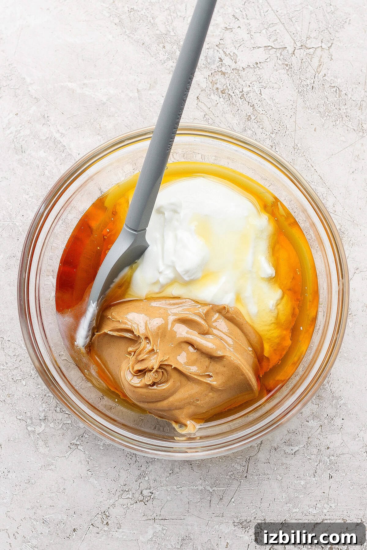 Creamy Peanut Butter Frozen Yogurt Bites Recipe 3 A glass bowl containing peanut butter, yogurt, honey, and an egg with a gray spatula resting inside.