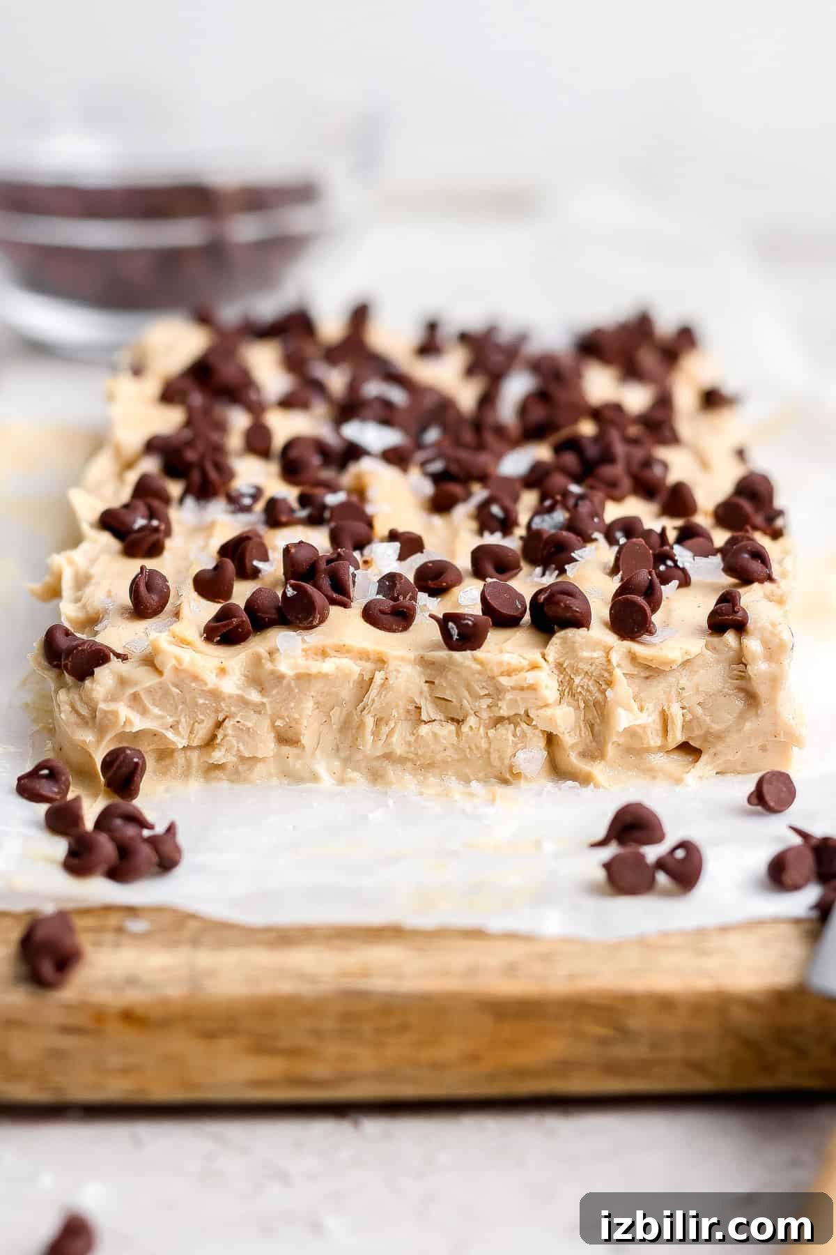 Creamy Peanut Butter Frozen Yogurt Bites Recipe 6 A slab of peanut butter fudge topped with chocolate chips sits on parchment paper on a wooden board.