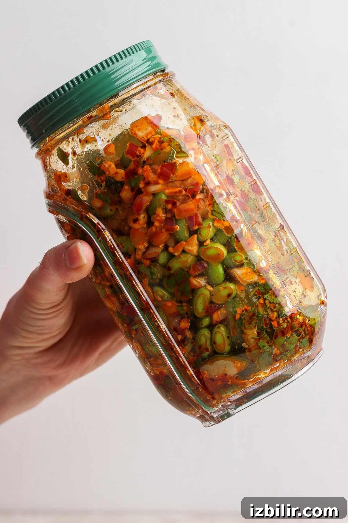 A hand holds a glass jar filled with colorful, chopped vegetables and spices, sealed with a green lid.