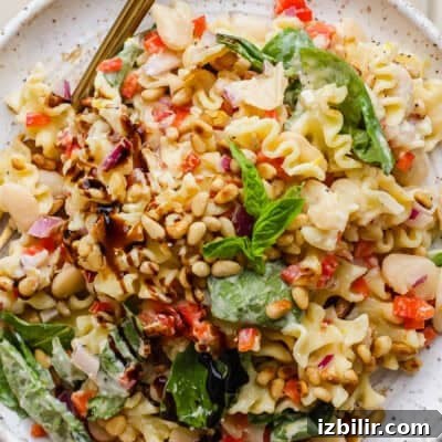 10 High-Protein Spring Recipes to Refresh Your Menu 11 A plate of pasta salad with spinach, pine nuts, white beans, chopped red onions, red bell peppers, and a balsamic drizzle, garnished with fresh basil.