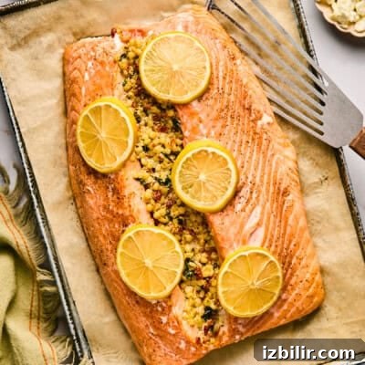 10 High-Protein Spring Recipes to Refresh Your Menu 7 A stuffed salmon fillet crowned with herbs and spices, garnished with lemon slices, rests on parchment paper on a baking tray beside a spatula.