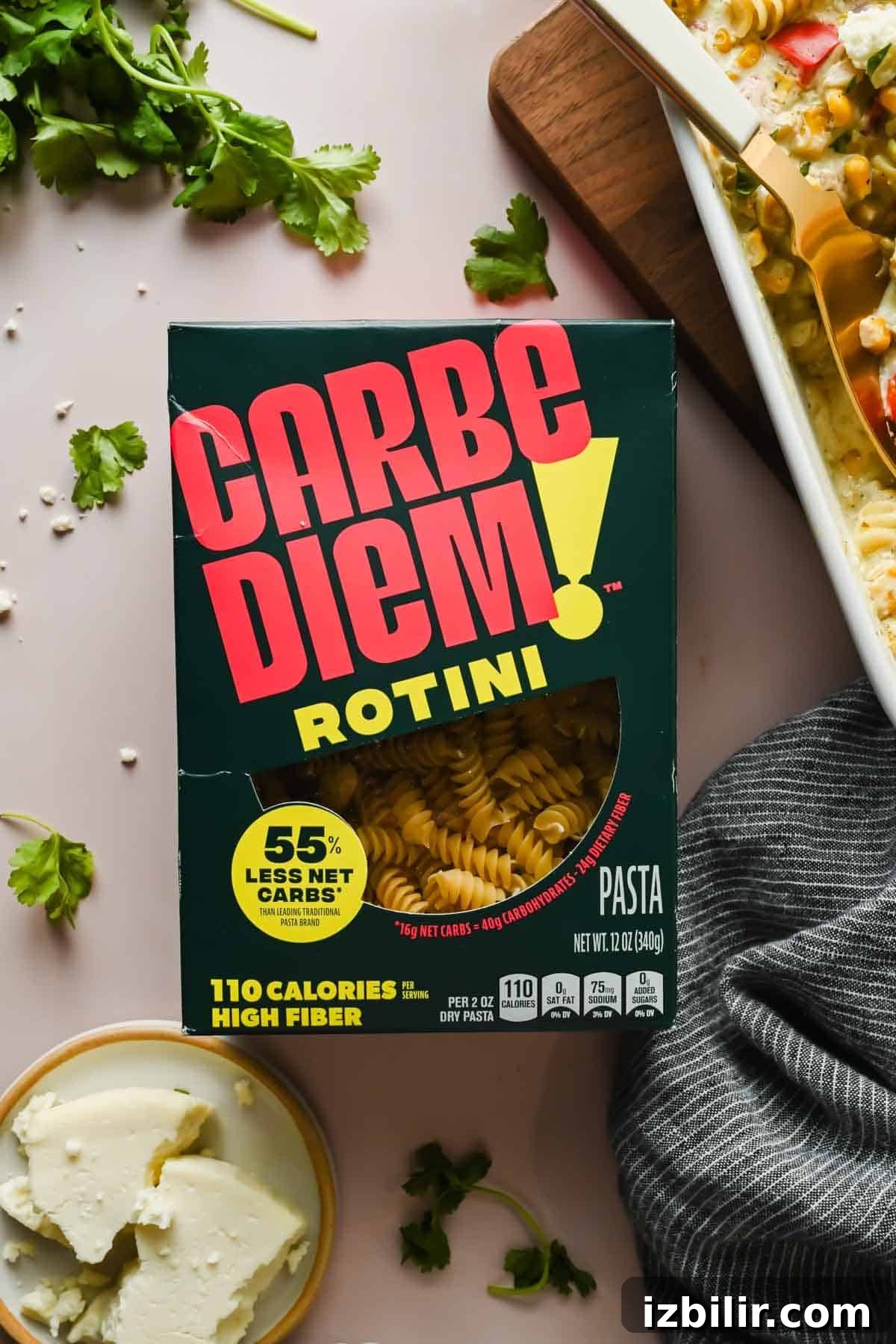 Creamy Oven Baked Street Corn Pasta with Cotija 4 A box of rotini pasta sits on a table next to a block of cheese, fresh parsley, and a dish of baked pasta.