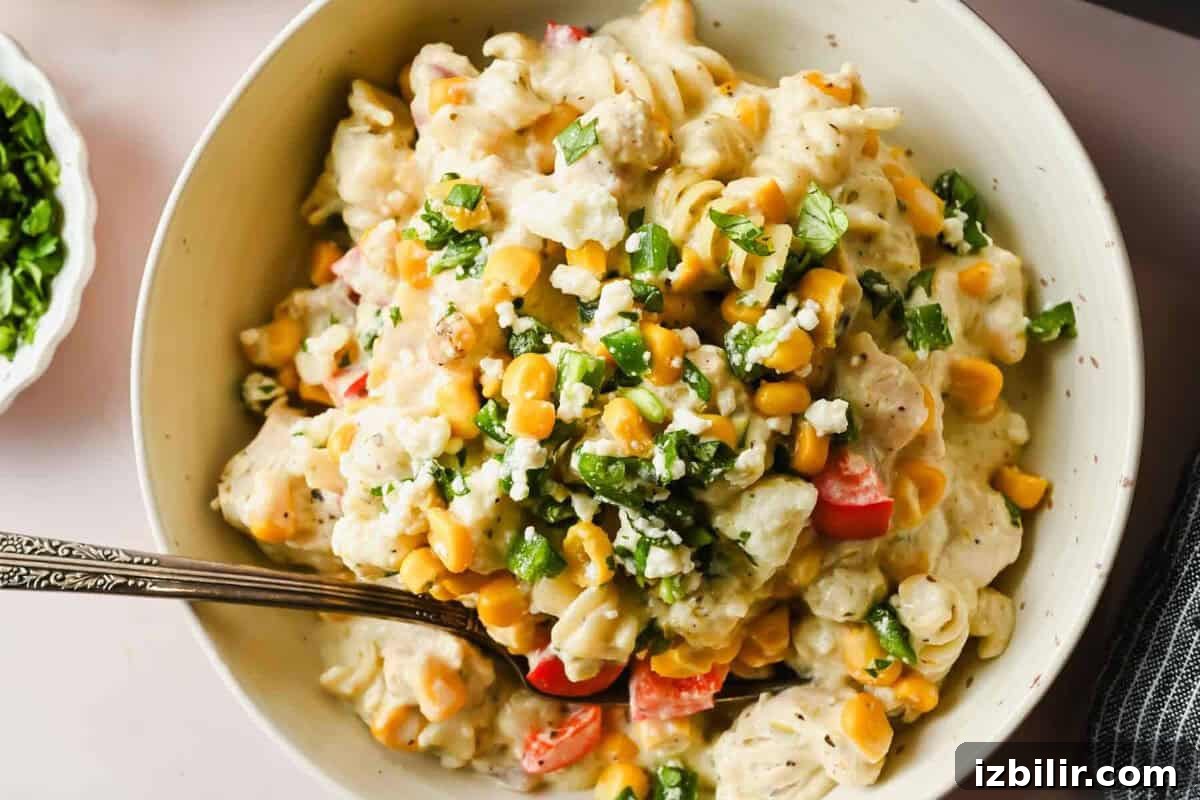 Creamy Oven Baked Street Corn Pasta with Cotija 6 Bowl of pasta salad with corn, chopped red bell peppers, crumbled cheese, and fresh herbs, served with a fork.