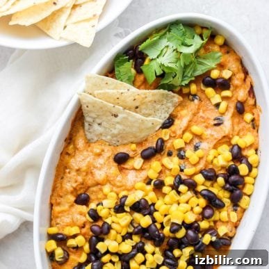 Street corn and queso dip in a white bowl with black beans.