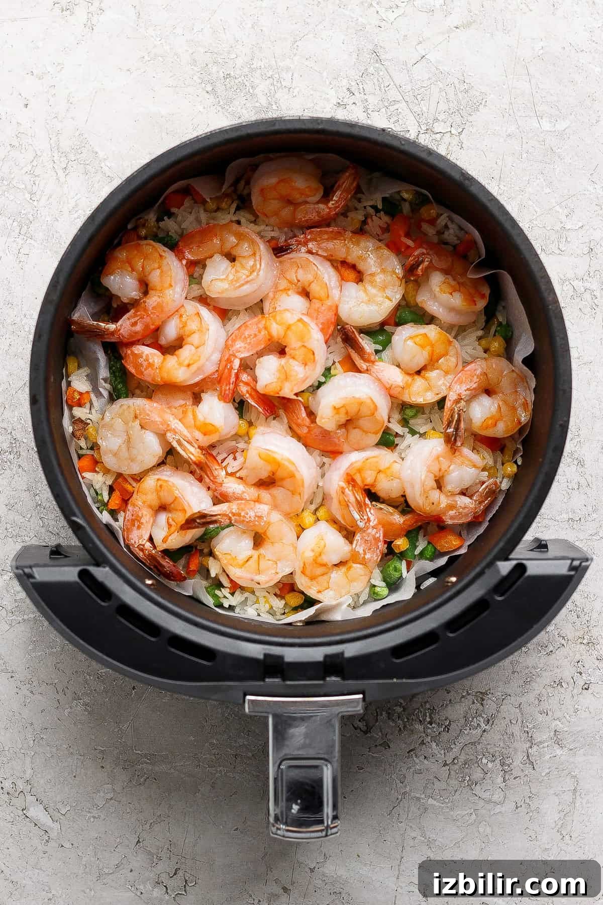 Raw shrimp and mixed vegetables arranged in a single layer inside an air fryer basket, ready to be cooked.