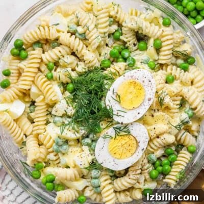 A bowl of fusilli pasta salad with green peas, chopped dill, and sliced hard-boiled egg halves on top.