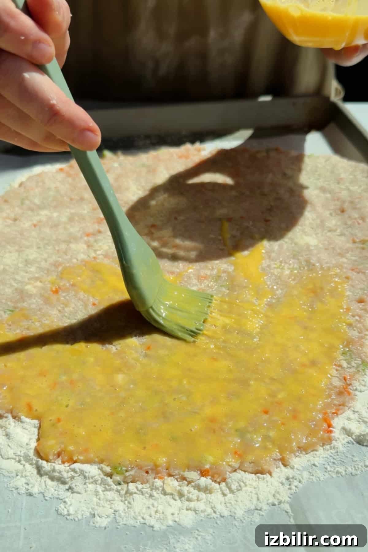 Brushing egg wash over chicken protein bar mixture on a floured parchment-lined surface