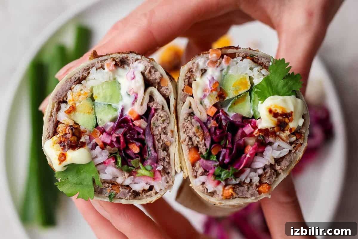 Close-up of a cut burrito filled with rice, ground meat, cucumber, egg, shredded vegetables, cilantro, and sauce