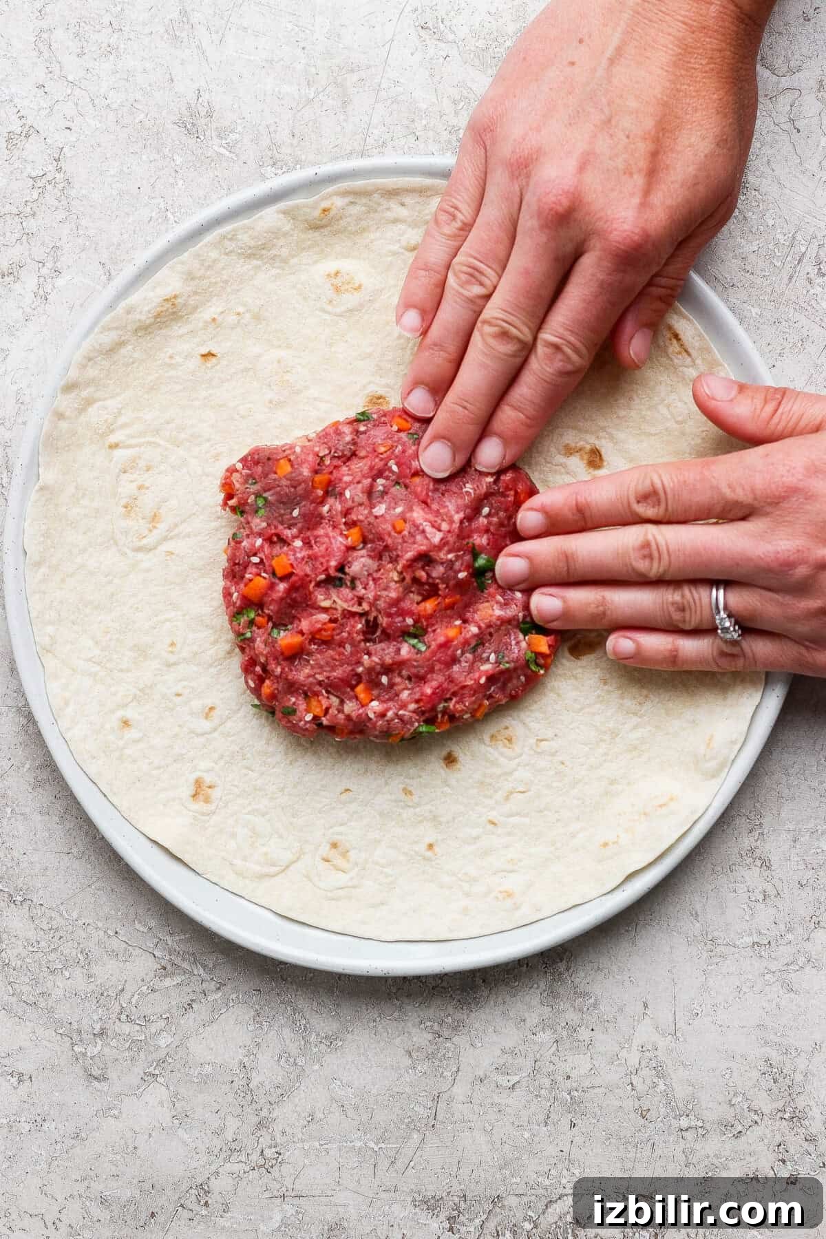 Hands pressing raw ground meat with vegetables onto a tortilla