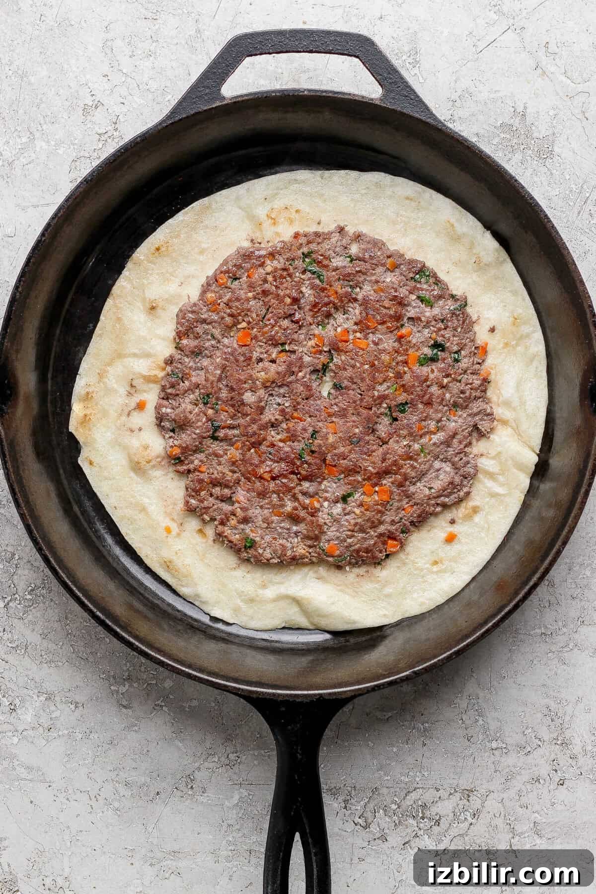 Cast iron skillet with tortilla topped with seasoned ground meat