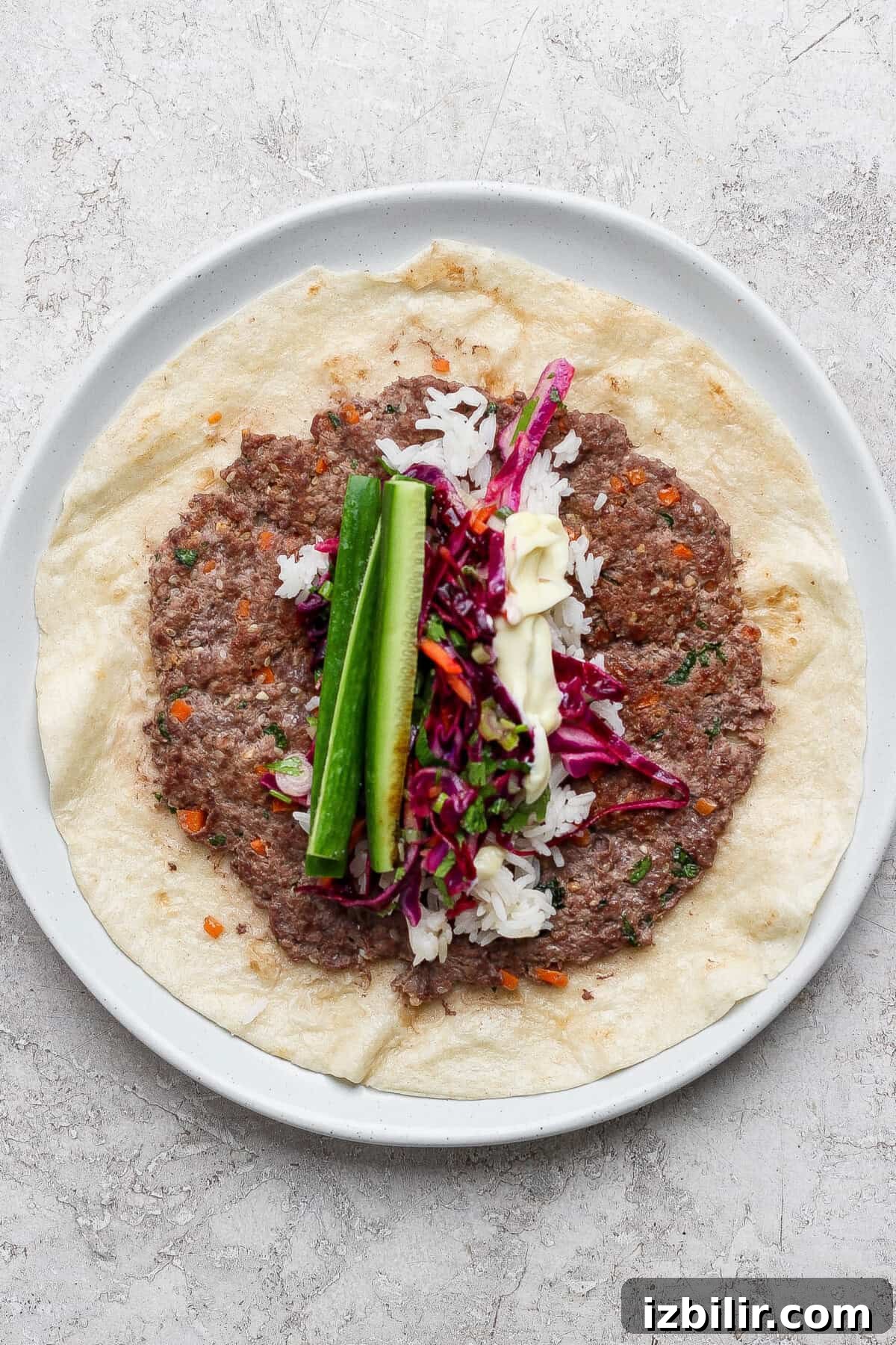 Flatbread topped with meat, rice, slaw, cucumber, and white sauce