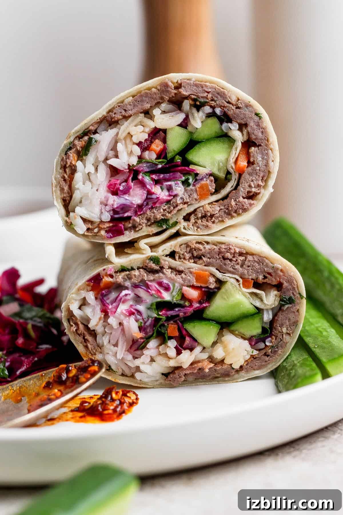 A halved wrap filled with rice, vegetables, and ground meat served on a white plate