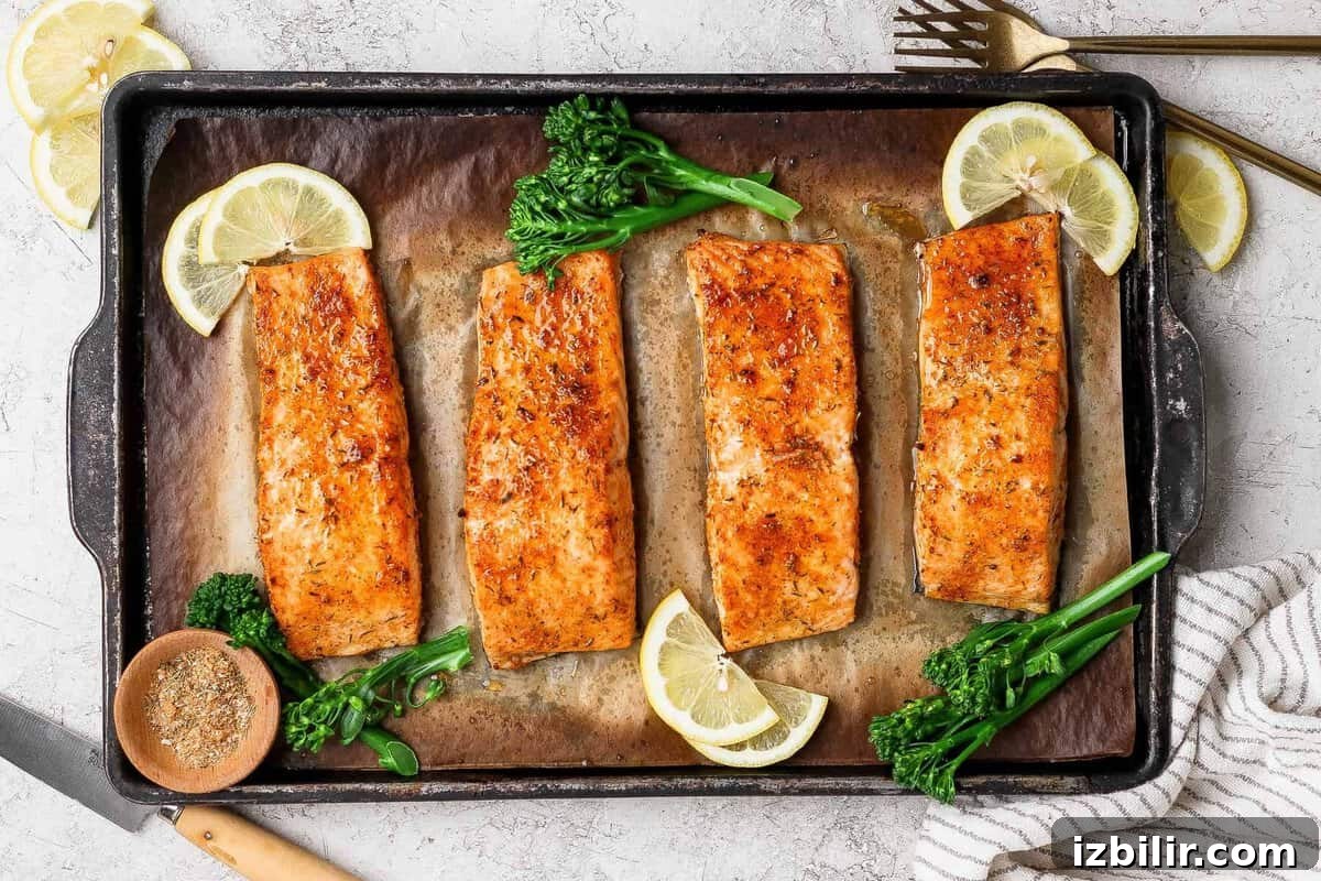 8-Minute Broiled Salmon with Simple Seasoning 2 Broiled salmon fillets on a baking sheet garnished with lemon slices, broccolini, and a bowl of seasoning.