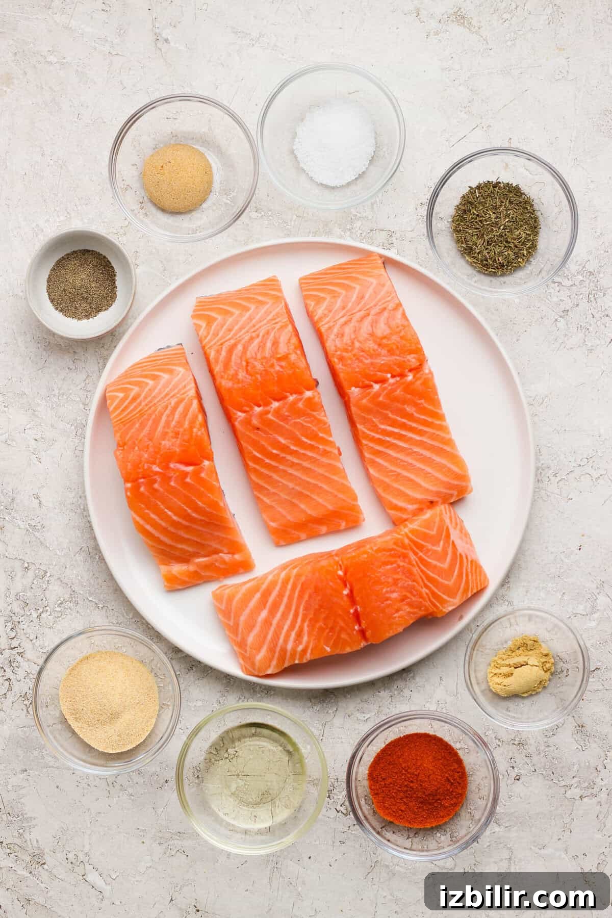 8-Minute Broiled Salmon with Simple Seasoning 3 Raw salmon fillets on a plate surrounded by small bowls of seasoning, avocado oil, and herbs.