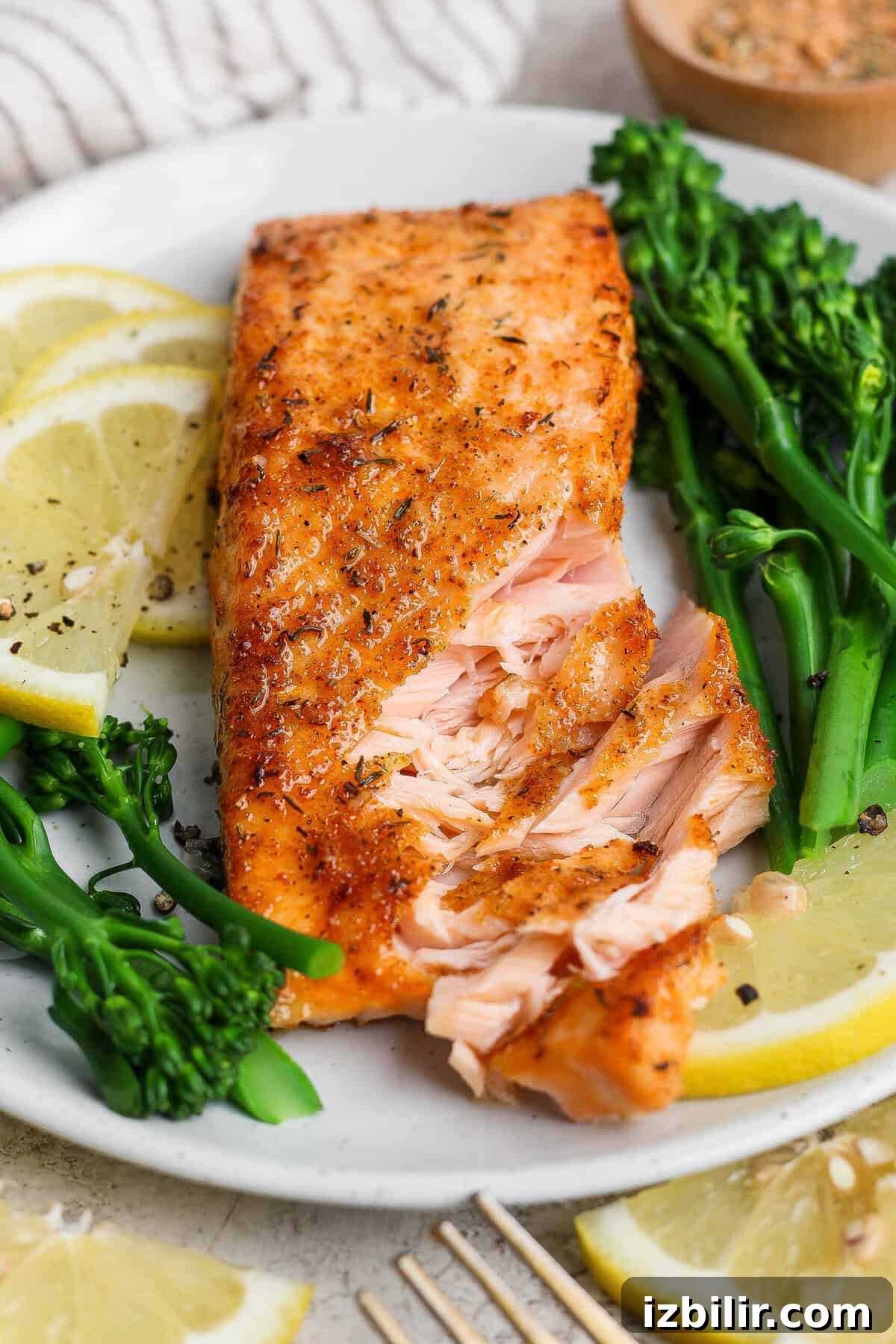 8-Minute Broiled Salmon with Simple Seasoning 7 Flaky broiled salmon fillet on a white plate with broccolini and lemon, showing the tender interior.