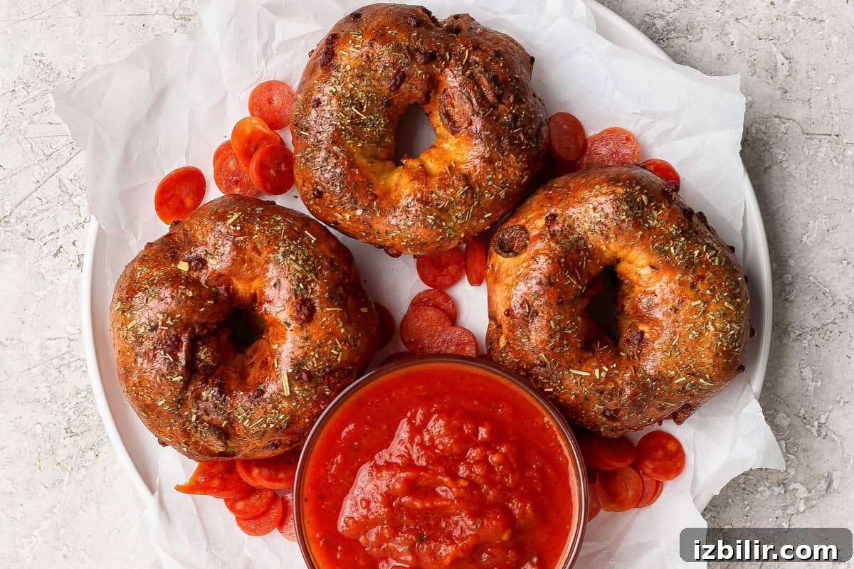 Three pizza protein bagels on parchment paper served with marinara sauce and pepperoni