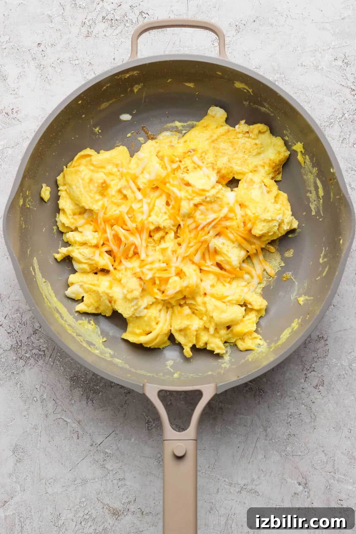 Scrambled eggs topped with shredded cheese in a nonstick skillet.